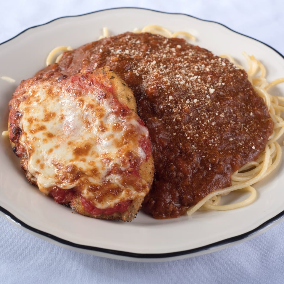 Chicken Parmesan with melted cheese and spaghetti with meat sauce, sprinkled with Parmesan cheese.