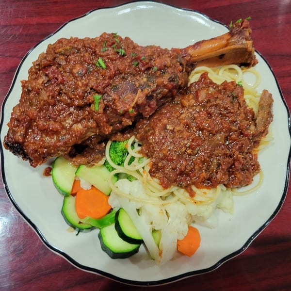Osso buco with spaghetti and mixed vegetables, including zucchini, carrots, broccoli, and cauliflower.